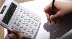 Photographie d'une main écrit sur une feuille blanche et l'autre tient une calculatrice